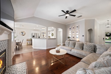 Living area featuring a tile fireplace, hardwood / wood-style floors, arched walkways, lofted ceiling, and a ceiling fan