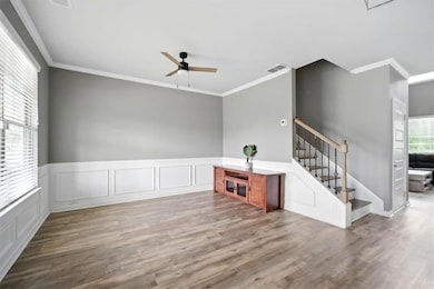 Unfurnished living room with ceiling fan, crown molding, wood finished floors, and stairs