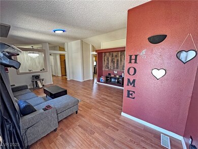 Living room with light wood finished floors, a textured wall, a textured ceiling, and vaulted ceiling