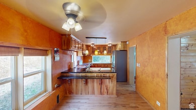 Kitchen with brown cabinets, a peninsula, freestanding refrigerator, light wood-style floors, and ceiling fan