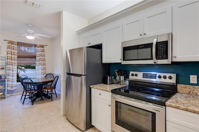 Kitchen featuring stainless steel appliances, light stone countertops, white cabinets, and ceiling fan