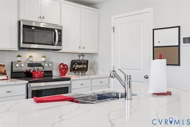 Kitchen featuring stainless steel appliances, white cabinets, and light stone countertops