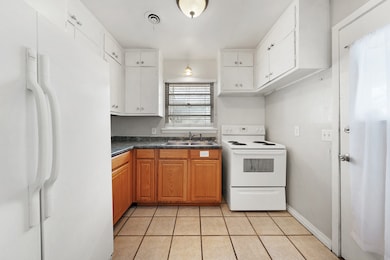 Kitchen featuring white appliances, light tile patterned floors, dark countertops, and brown cabinets