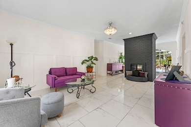 Living room featuring a decorative wall, marble finish flooring, a brick fireplace, a wainscoted wall, and crown molding