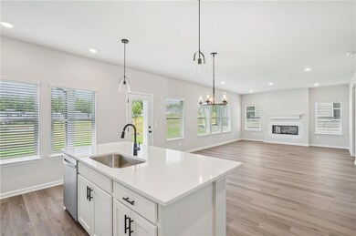 Kitchen with dishwasher, light wood-style floors, pendant lighting, a kitchen island with sink, and white cabinets