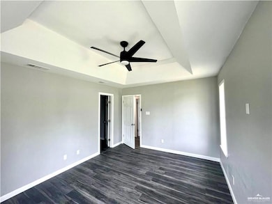 Empty room featuring dark hardwood / wood-style floors, ceiling fan, and a tray ceiling