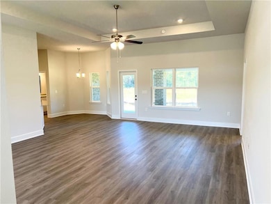 Unfurnished living room featuring dark wood-style flooring, a raised ceiling, a chandelier, and ceiling fan