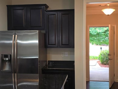 Kitchen with stainless steel fridge with ice dispenser, dark stone countertops, wood finished floors, and dark cabinetry