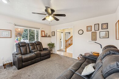 Carpeted living room with ceiling fan and stairway