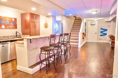 Indoor wet bar with a drop ceiling, light stone countertops, stairway, light wood finished floors, and stainless steel dishwasher