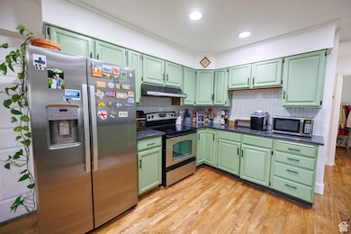 Kitchen with green cabinetry, stainless steel appliances, tasteful backsplash, light wood finished floors, and ornamental molding