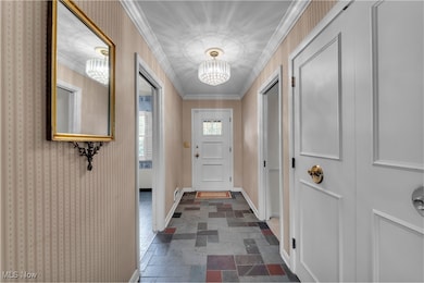 Doorway to outside with crown molding, stone tile floors, and a chandelier