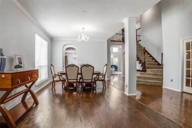 Dining room featuring crown molding, arched walkways, a chandelier, dark wood-style floors, and stairs