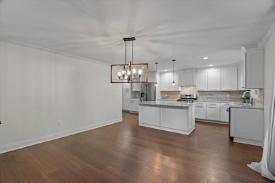 Kitchen with tasteful backsplash, a chandelier, a center island, decorative light fixtures, and ornamental molding