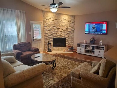 Living area featuring vaulted ceiling, a fireplace, wood finished floors, and a ceiling fan