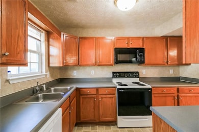 Kitchen featuring white dishwasher, a sink, electric range oven, black microwave, and a textured ceiling