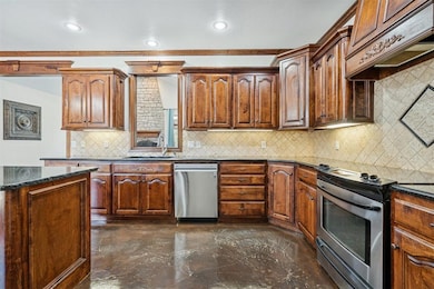 Kitchen featuring stainless steel appliances, backsplash, dark stone counters, custom range hood, and brown cabinets