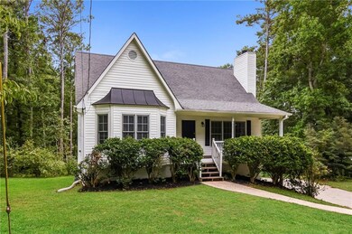 View of front facade with a standing seam roof, a front yard, a porch, a chimney, and metal roof