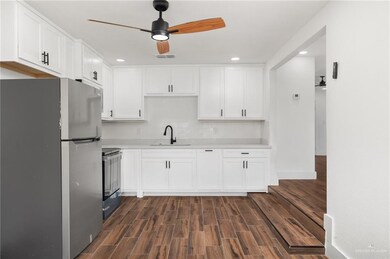 Kitchen featuring dark wood-type flooring, sink, appliances with stainless steel finishes, decorative backsplash, and white cabinets