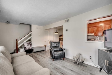 Living room featuring light wood-style flooring, stairs, a textured ceiling, and baseboards
