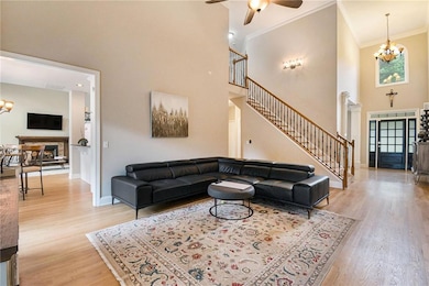 Living area with stairs, ceiling fan, light wood-style floors, a towering ceiling, and crown molding
