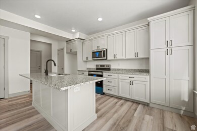 Kitchen with light wood-style flooring, appliances with stainless steel finishes, an island with sink, and a sink
