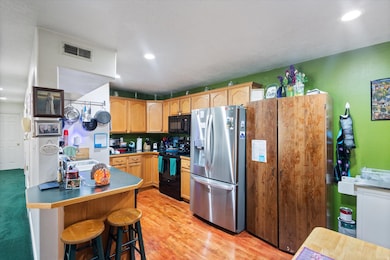 Kitchen with black appliances, a kitchen bar, light wood-style flooring, recessed lighting, and a peninsula