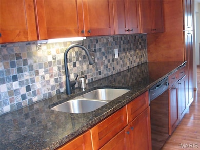 Kitchen featuring backsplash, dark stone countertops, light wood-style flooring, and dishwasher