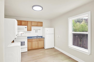 Kitchen with white appliances, decorative backsplash, light wood-style flooring, and light countertops
