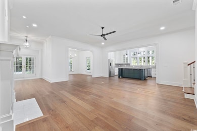 Unfurnished living room featuring ceiling fan, ornamental molding, light wood-style flooring, stairway, and recessed lighting