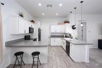 Kitchen featuring a peninsula, a kitchen breakfast bar, white cabinets, wood tiled floors, and recessed lighting