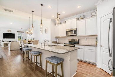 Kitchen featuring backsplash, appliances with stainless steel finishes, light wood finished floors, a kitchen bar, and light stone counters
