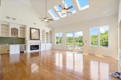 Unfurnished living room featuring high vaulted ceiling, built in shelves, light wood-type flooring, and a skylight