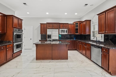 Kitchen with stainless steel appliances, a sink, dark stone countertops, crown molding, and glass insert cabinets