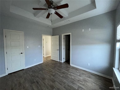 Unfurnished bedroom with a tray ceiling, dark wood-style flooring, and ceiling fan