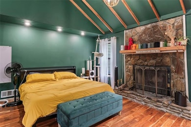 Bedroom featuring wood finished floors, beamed ceiling, high vaulted ceiling, and a fireplace