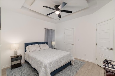 Bedroom with light wood-style floors, a ceiling fan, and a raised ceiling