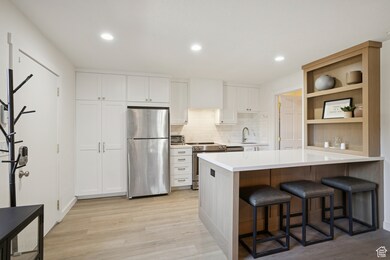 Kitchen with a kitchen bar, tasteful backsplash, a peninsula, stainless steel appliances, and white cabinetry