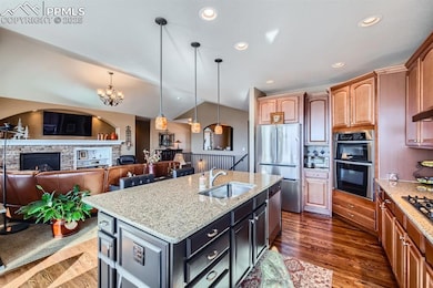 Kitchen featuring sink, light stone counters, a center island with sink, stainless steel appliances, and a fireplace