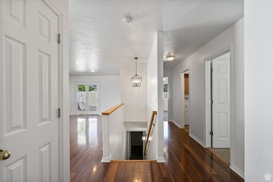 Corridor featuring an upstairs landing, a textured ceiling, dark wood-style flooring, and a chandelier