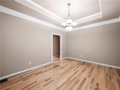 Unfurnished room featuring a tray ceiling, ornamental molding, light wood-style flooring, and a chandelier