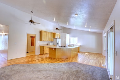 Kitchen with open floor plan, light countertops, light wood-style flooring, an island with sink, and white appliances