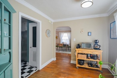 Hallway with arched walkways, baseboards, wood finished floors, and crown molding
