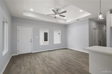 Unfurnished living room with a tray ceiling, dark wood-type flooring, ceiling fan, recessed lighting, and plenty of natural light