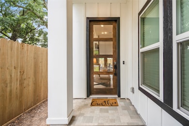 A covered patio, modern glass front door and paved patio to enter from the iron gate.