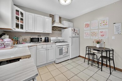 Kitchen featuring white gas stove, wall chimney exhaust hood, decorative backsplash, light countertops, and glass insert cabinets