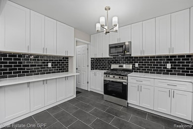 Kitchen featuring appliances with stainless steel finishes, white cabinetry, light stone countertops, and pendant lighting