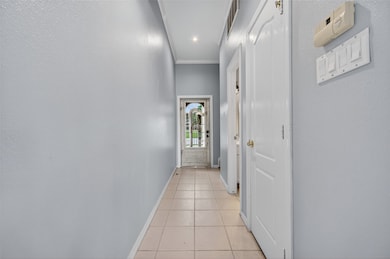 This photo shows a bright, narrow hallway with light-colored walls and tile flooring, leading to a glass-paned door. It features several doors on the right side and has overhead lighting.