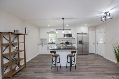 Kitchen with light parquet floors, backsplash, appliances with stainless steel finishes, dark countertops, decorative light fixtures, white cabinetry, and a center island