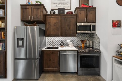 Kitchen featuring stainless steel appliances, decorative backsplash, dark brown cabinets, and finished concrete floors